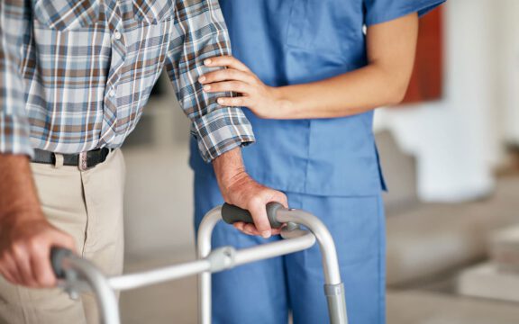 Caregiver supporting elderly man using a walker indoors